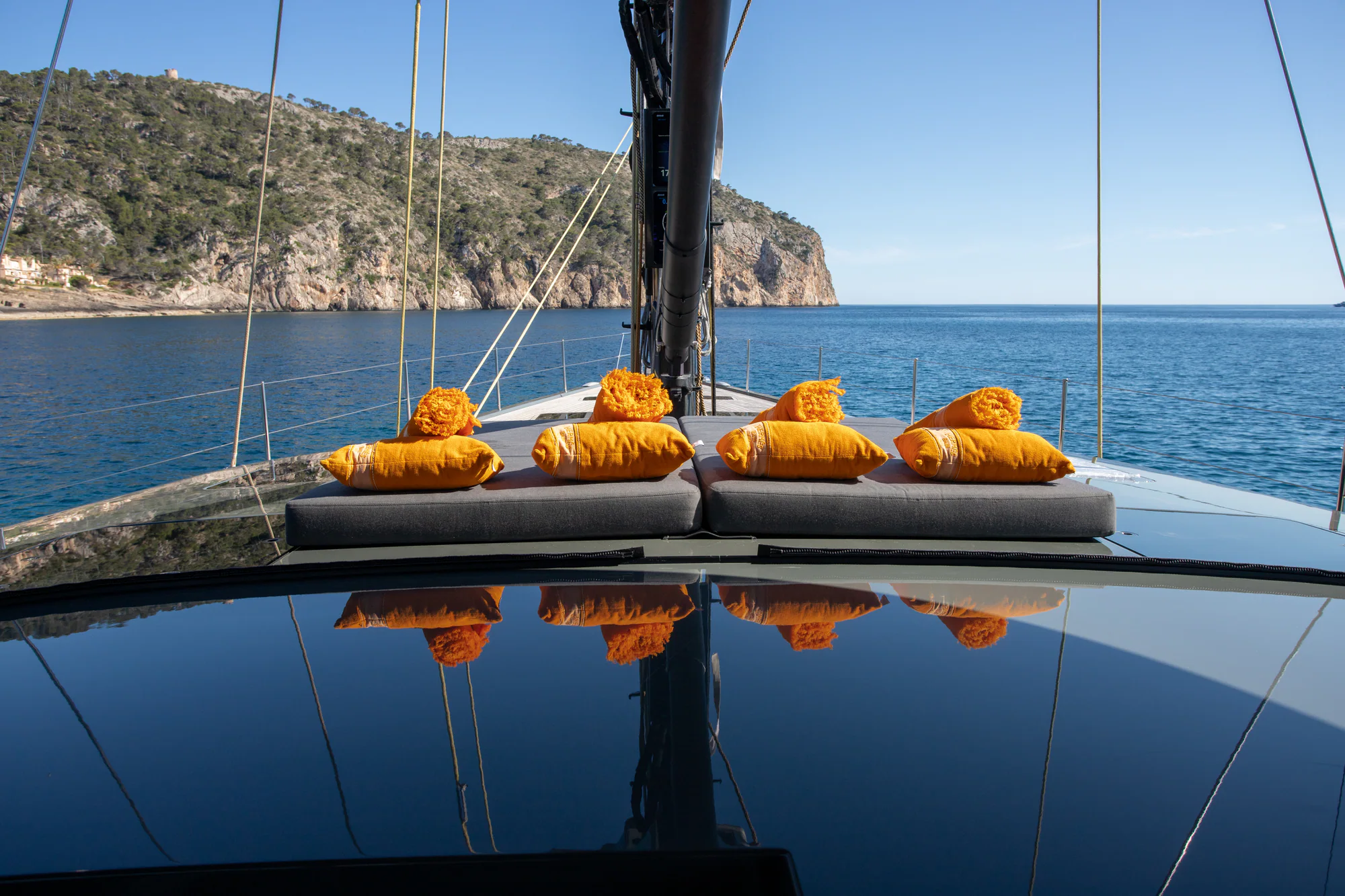 Forward sunpads with cushions on the foredeck of Sailing Yacht W, a quiet Mediterranean cove beyond