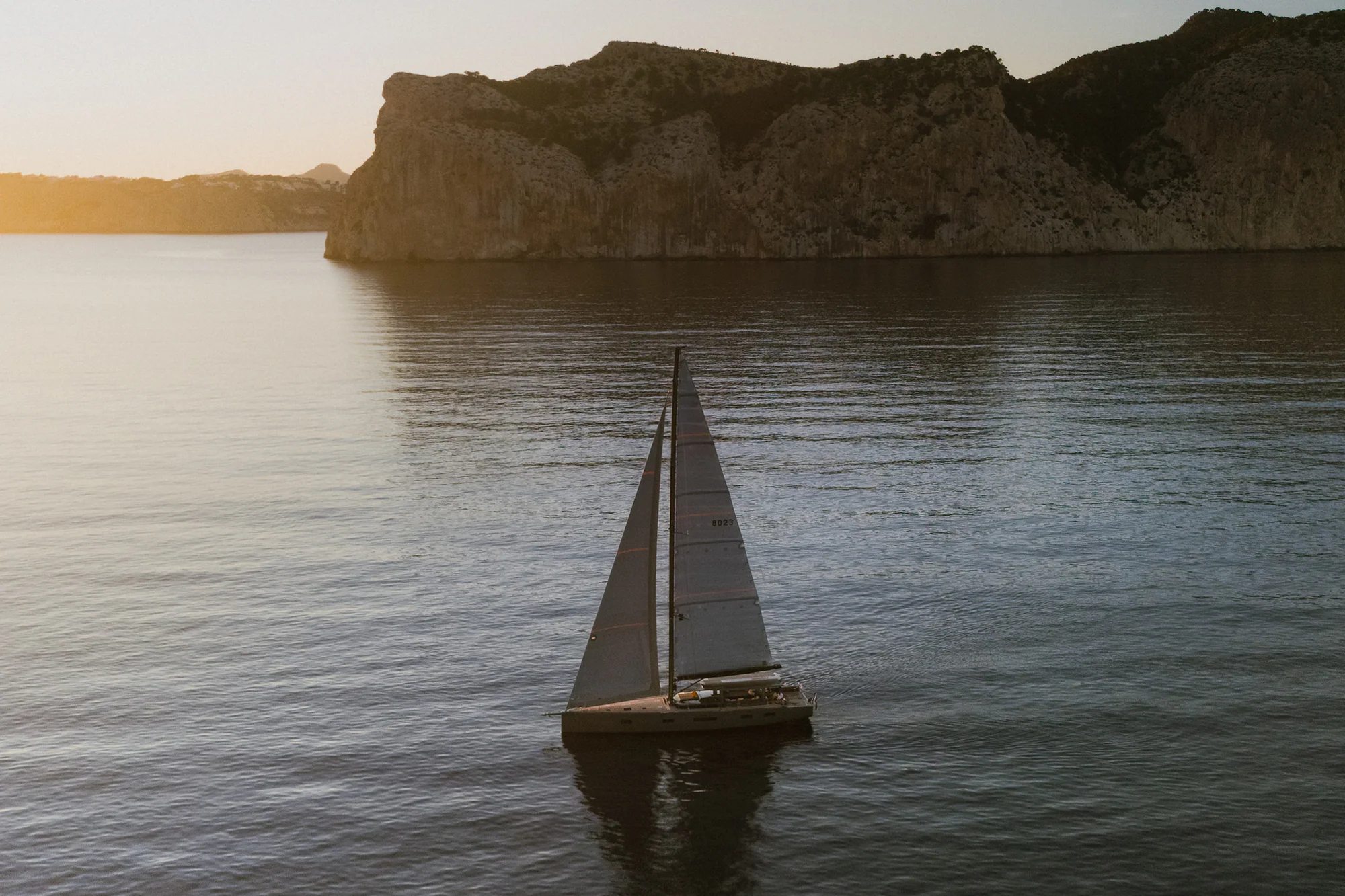 Sailing Yacht W sailing a remote stretch of coast at sunset