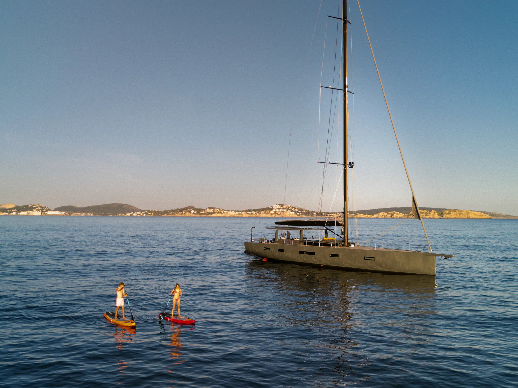 Paddleboarding in a calm Mediterranean bay beside Sailing Yacht W